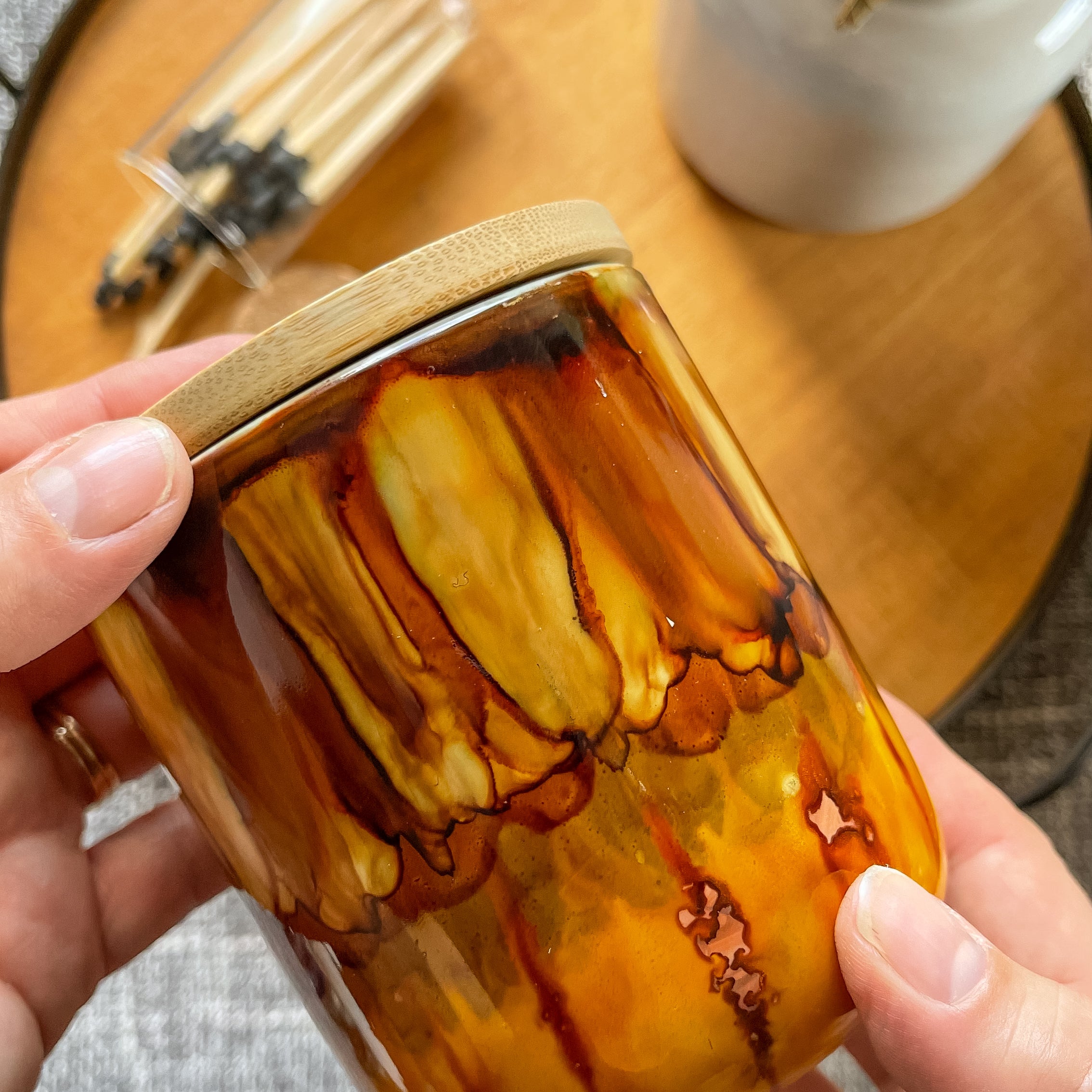 Hand holding a tall handpainted candle in shades of brown, amber, and deep yellow
