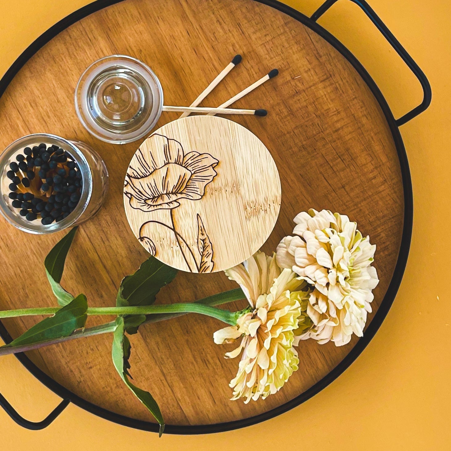 Top view of a all candle with a laser engraved bamboo lid on a tray with flowers and matches