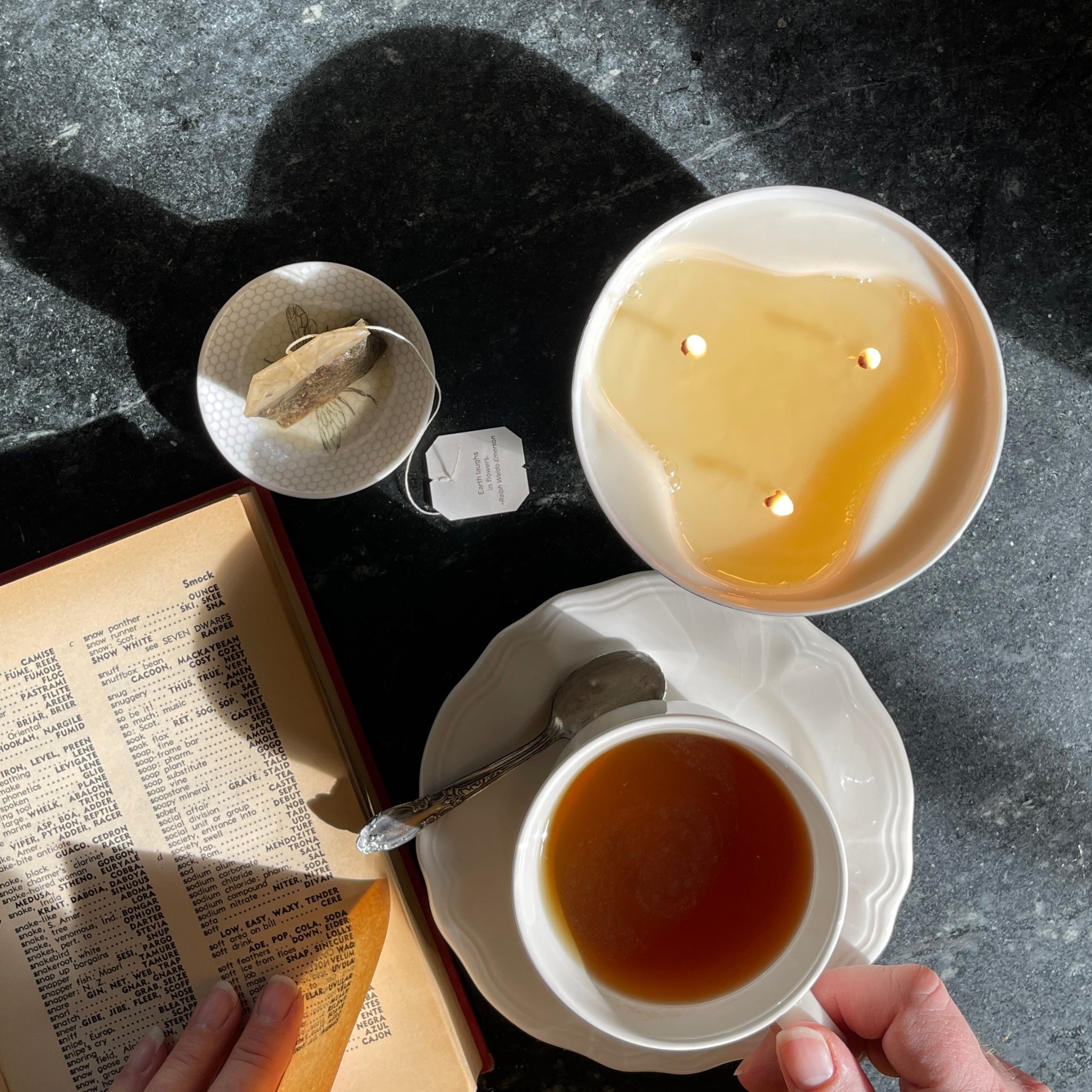 Top view of a lit three wick candle with a book and a cup of hot tea