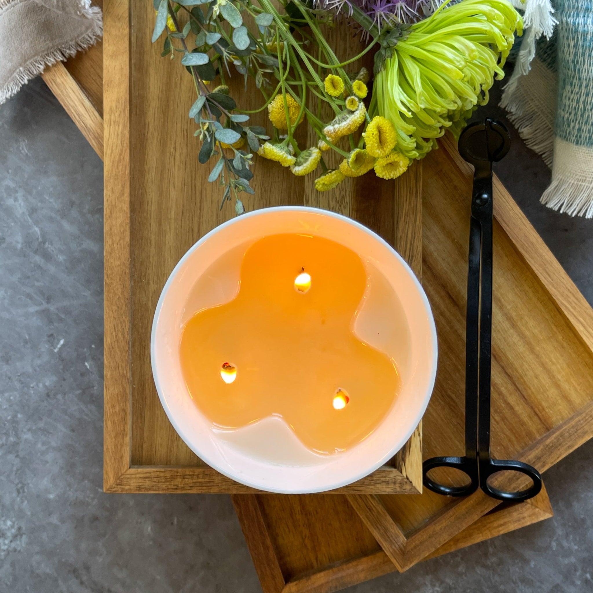 Top view of a three wick ceramic candle and wick trimmers on a tray with flowers