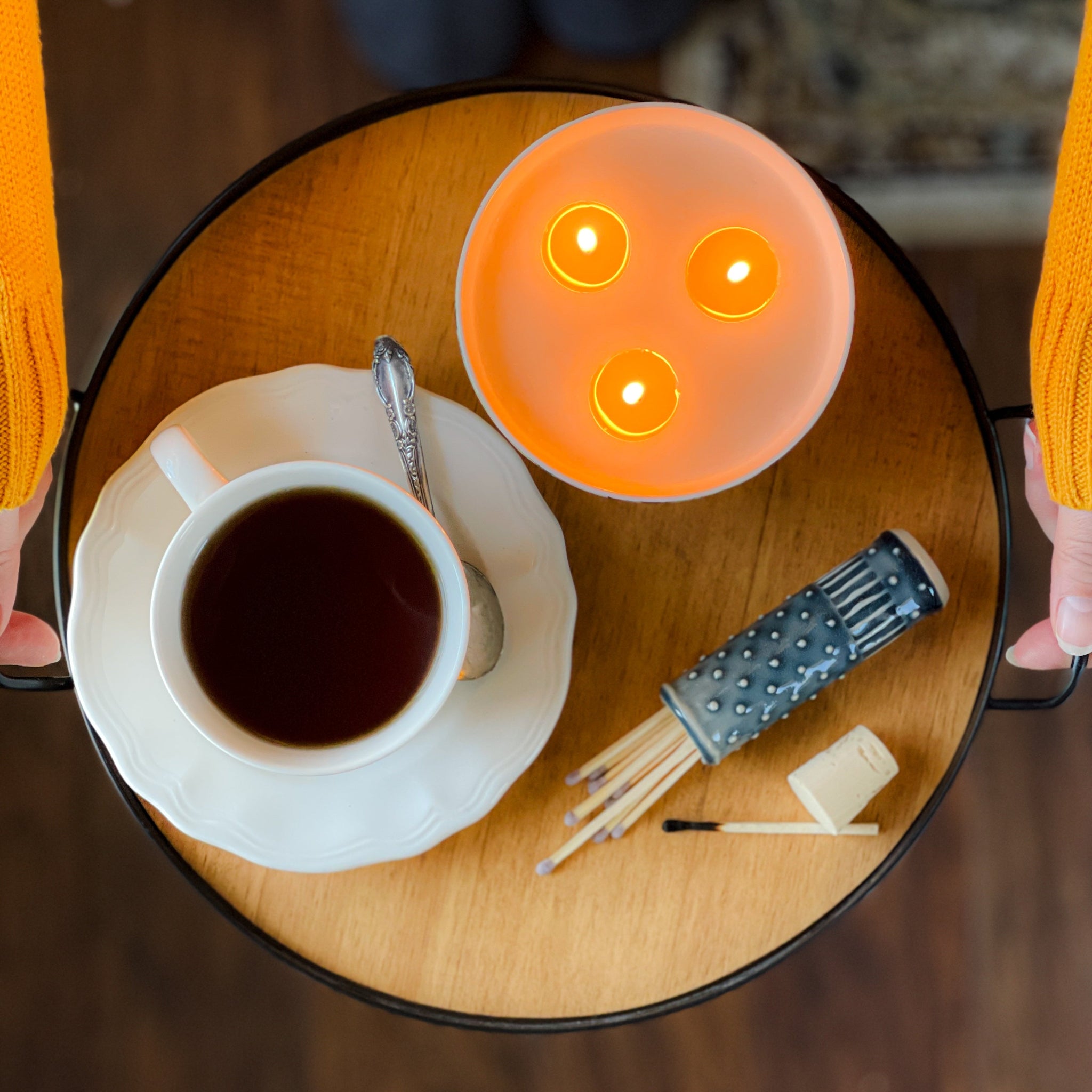 Top view of a lit three wick candle on a tray with matches and a teacup