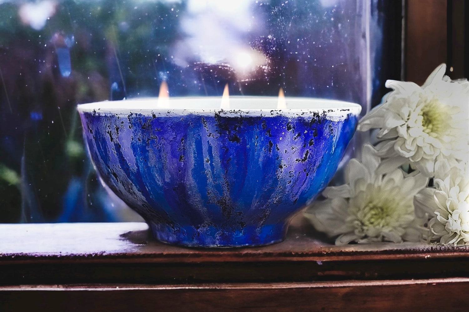 Bright blue handpainted ceramic candle burning by a rainy window