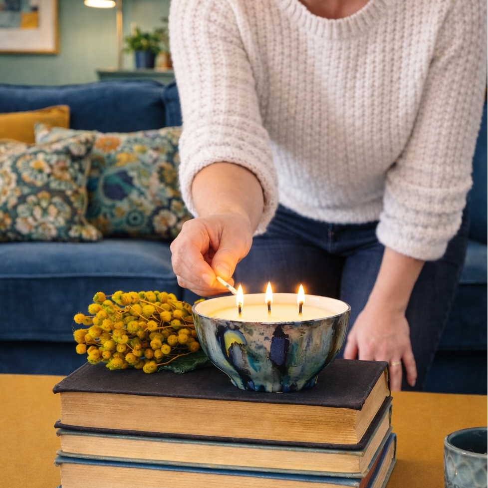 A woman lighting a three wick handpainted candle on a stack of books