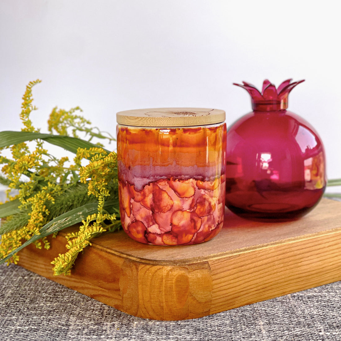 Tall, two wick ceramic soy candle handpainted in shades of red, raspberry, deep orange, and a touch of purple