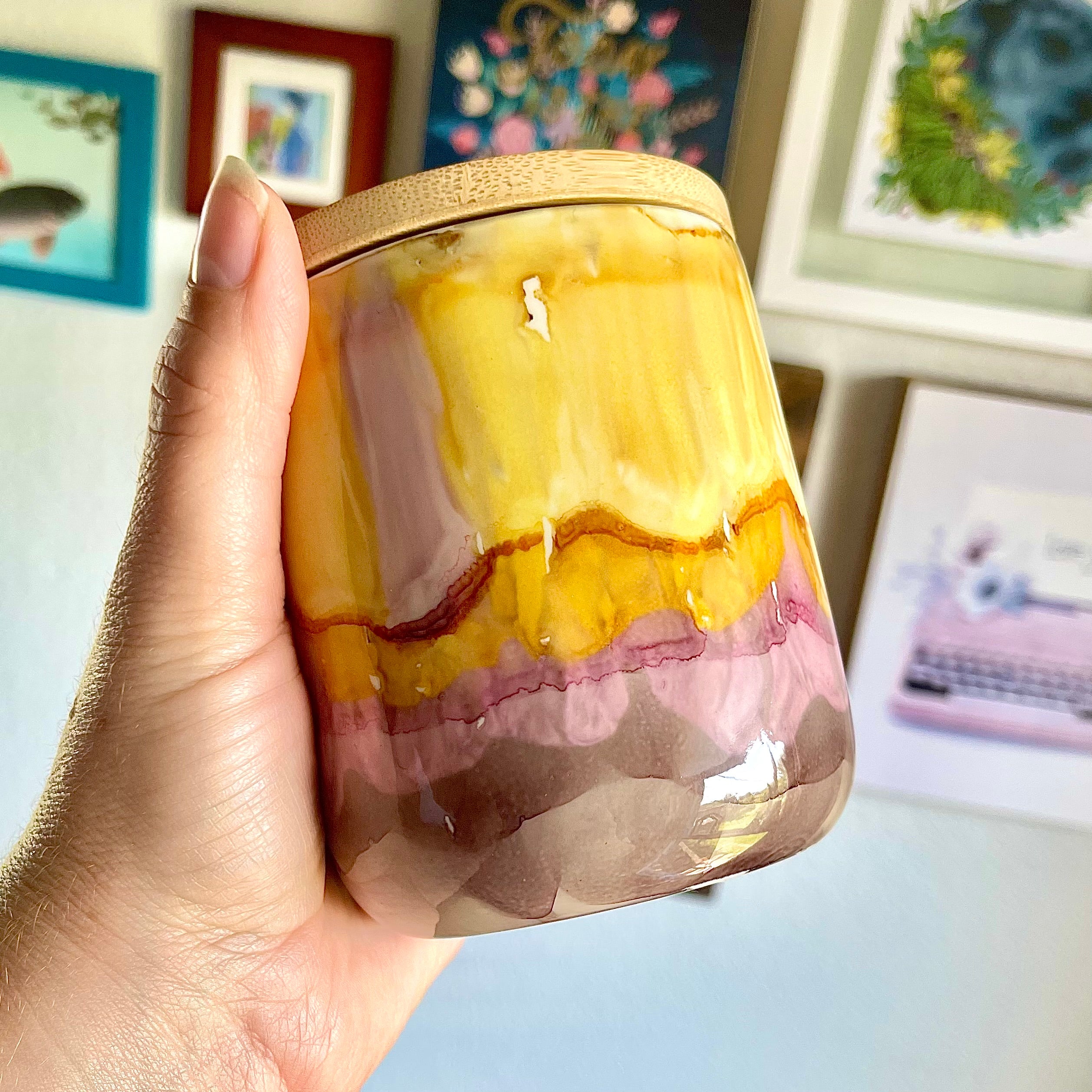 Hand holding a tall, two wick ceramic soy candle handpainted in layers of gray, soft pink, amber, and yellow