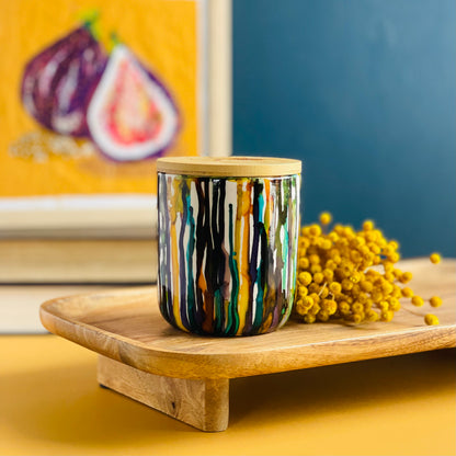 Tall, two wick ceramic soy candle handpainted in drippy yellows, warm browns, with touches of leafy green, teal and wine purple