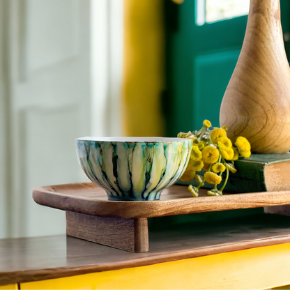 Ceramic three wick soy candle handpainted in greens, blues, and teals set on an entry table