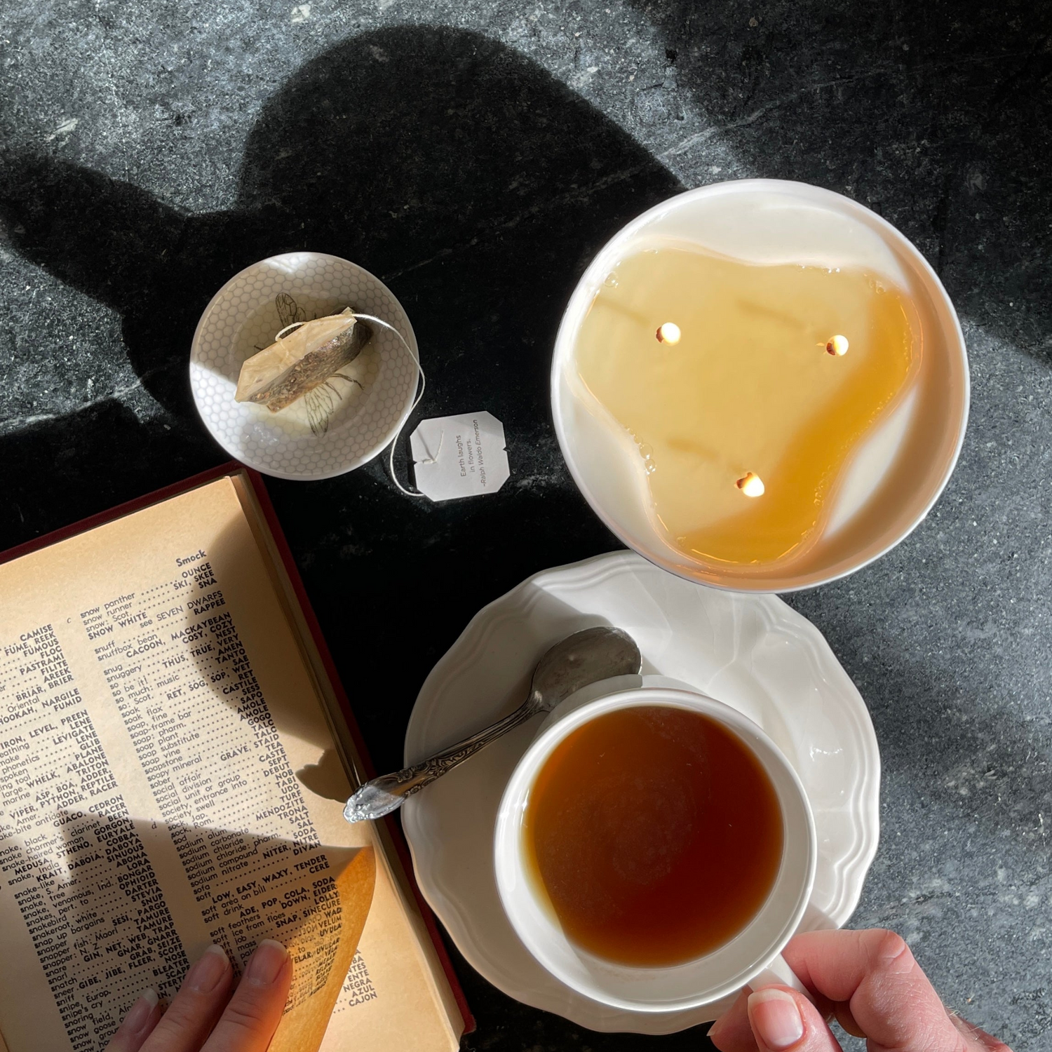 Top view of a lit three wick candle with a book and a cup of hot tea