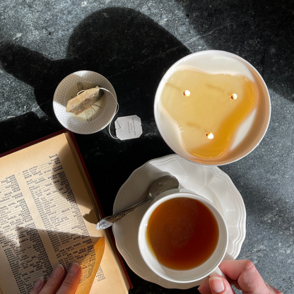 Top view of a lit three wick candle with a book and a cup of hot tea