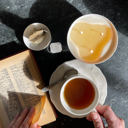 Top view of a three wick ceramic candle with a book and a cup of tea