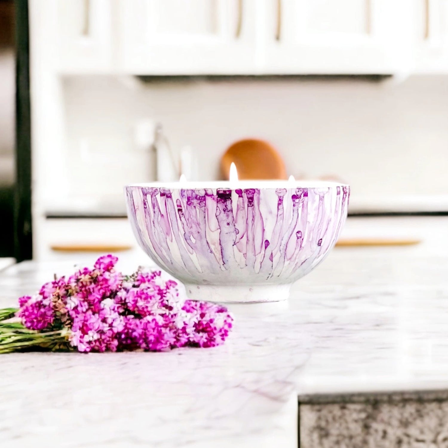 Ceramic three wick soy candle handpainted in shades of lilac lit on a kitchen counter
