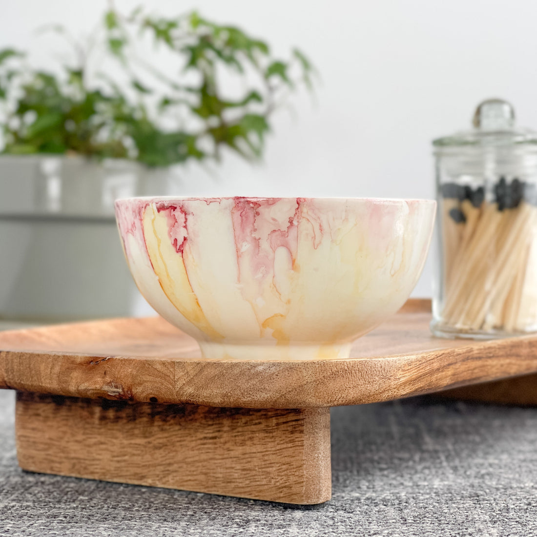 A hand-painted candle with hues of pink, yellow, and red sitting on a wood tray.